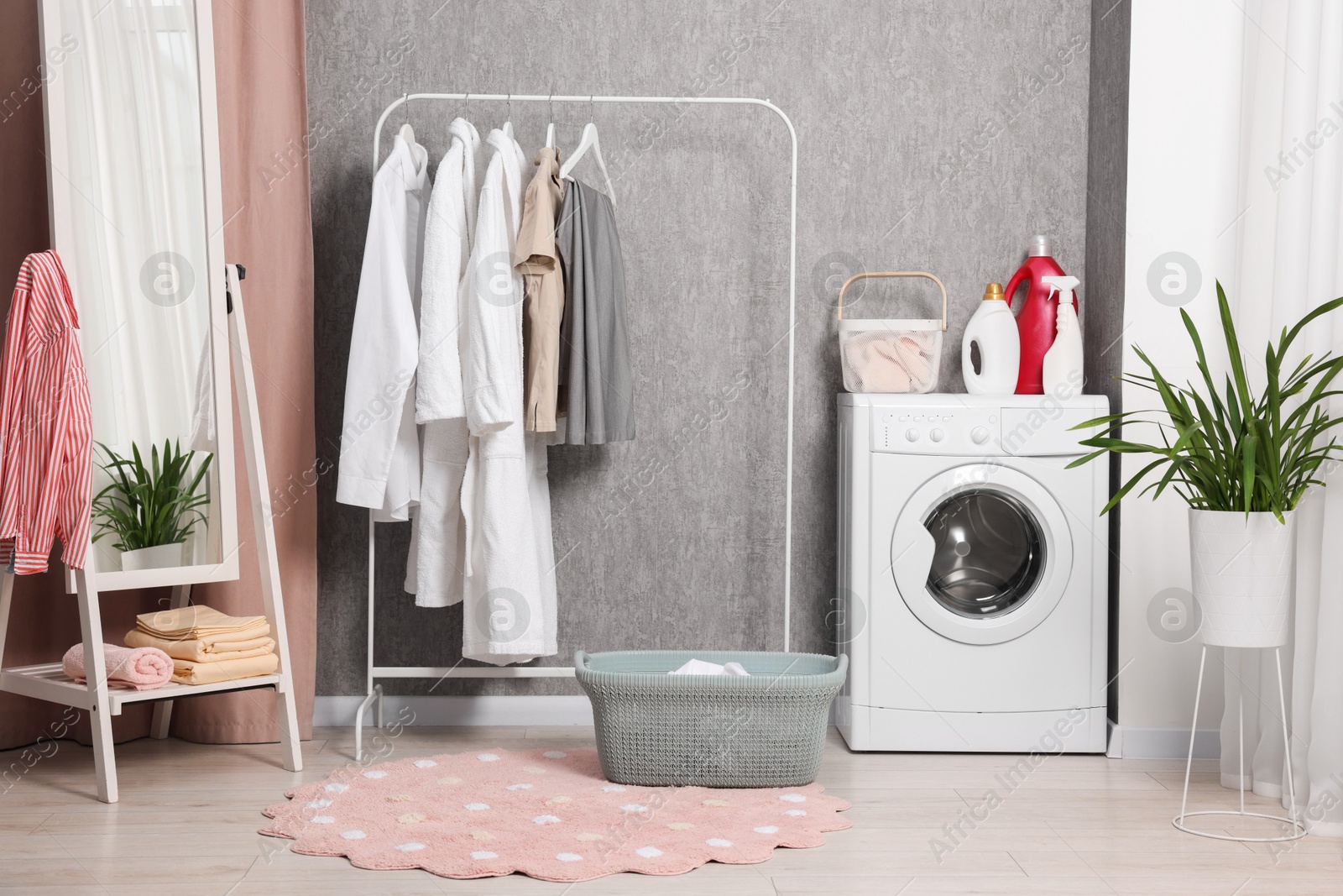 Photo of Washing machine, detergents, baskets, clothing rack and mirror indoors