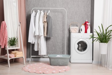 Photo of Washing machine, detergents, baskets, clothing rack and mirror indoors