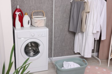 Photo of Washing machine, detergents, baskets and clothing rack indoors