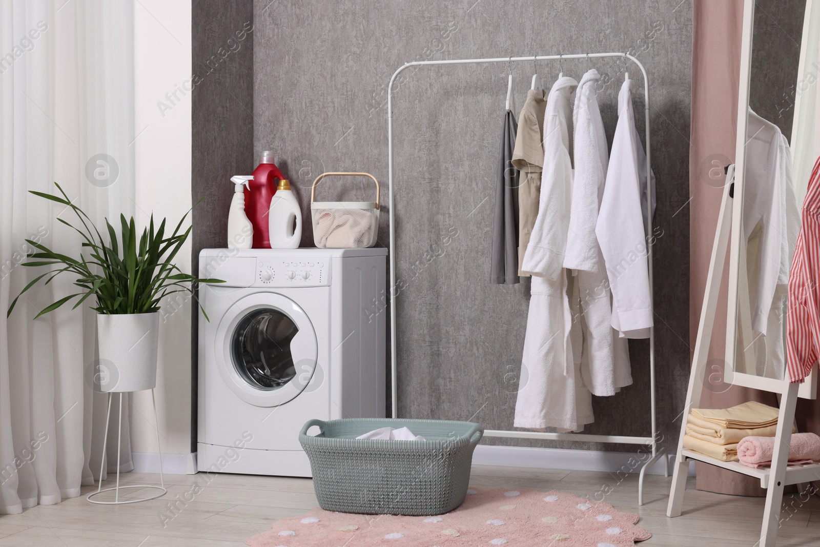 Photo of Washing machine, detergents, baskets, clothing rack and mirror indoors