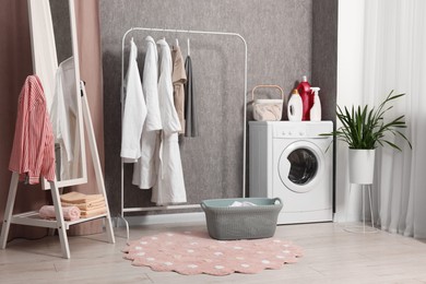 Photo of Washing machine, detergents, baskets, clothing rack and mirror indoors