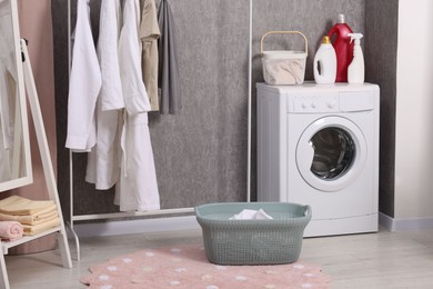 Photo of Washing machine, detergents, baskets, clothing rack and mirror indoors