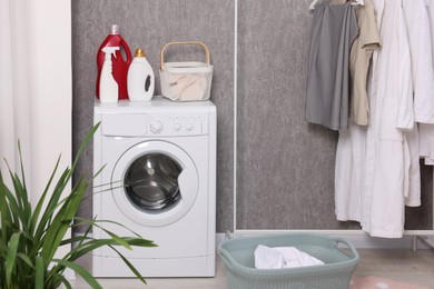 Photo of Washing machine, detergents, baskets, clothing rack and houseplant indoors