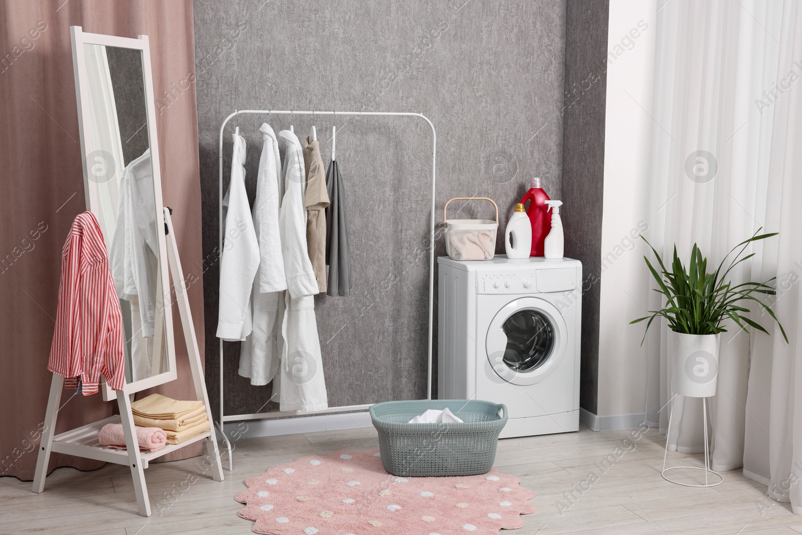 Photo of Washing machine, detergents, baskets, clothing rack and mirror indoors