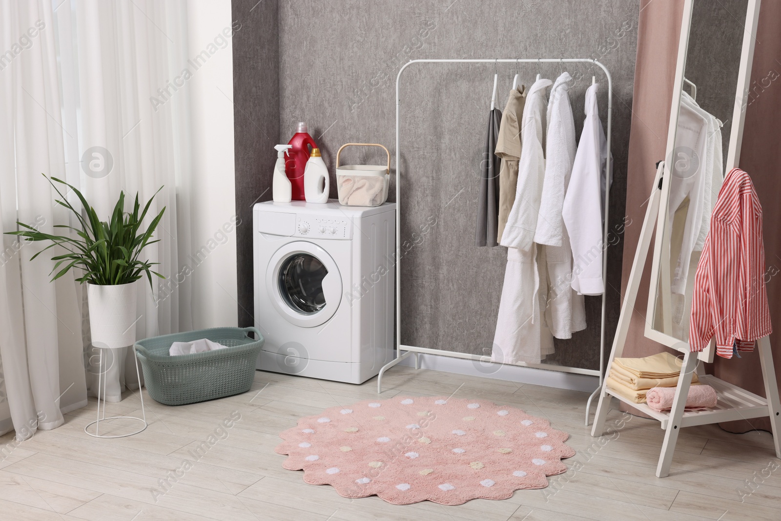 Photo of Washing machine, detergents, baskets, clothing rack and mirror indoors