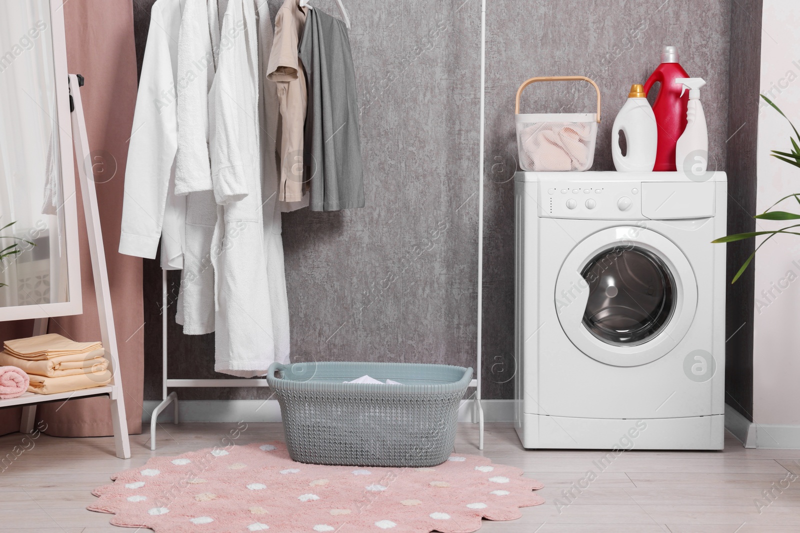 Photo of Washing machine, detergents, baskets, clothing rack and mirror indoors