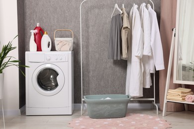 Photo of Washing machine, detergents, baskets, clothing rack and mirror indoors