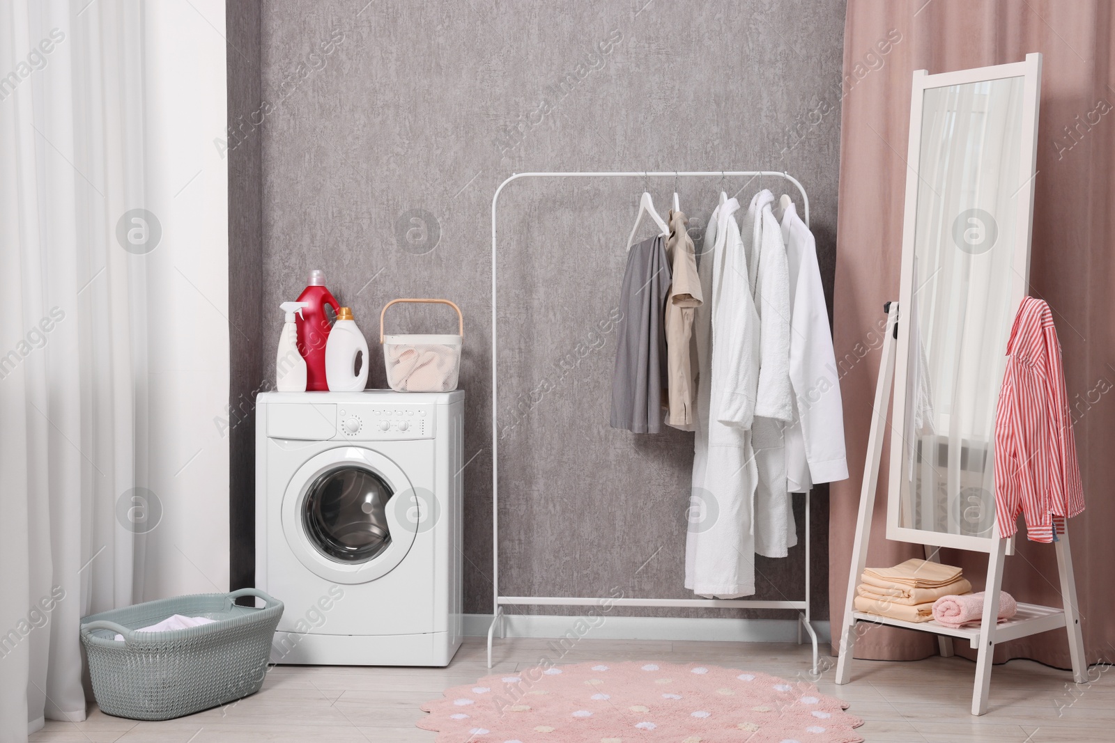 Photo of Washing machine, detergents, baskets, clothing rack and mirror indoors