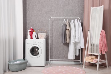 Photo of Washing machine, detergents, baskets, clothing rack and mirror indoors