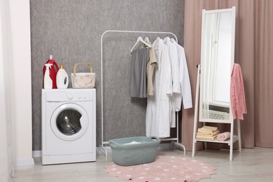 Photo of Washing machine, detergents, baskets, clothing rack and mirror indoors