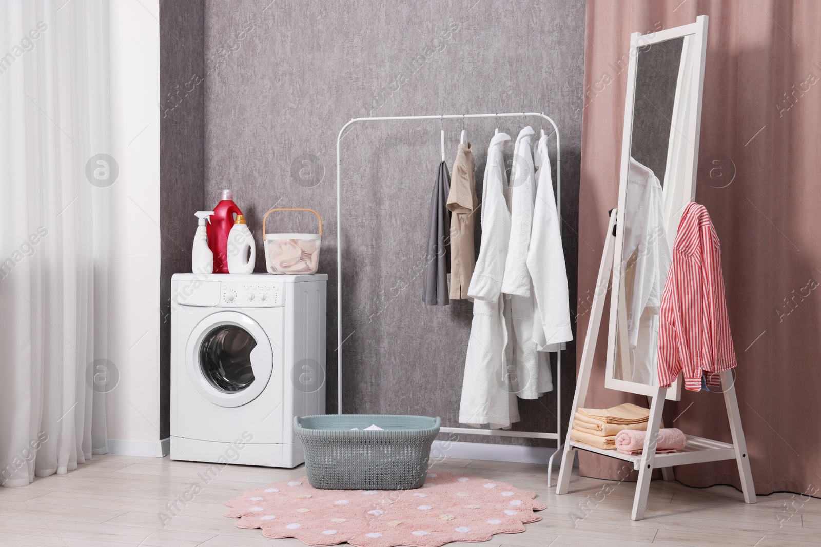 Photo of Washing machine, detergents, baskets, clothing rack and mirror indoors