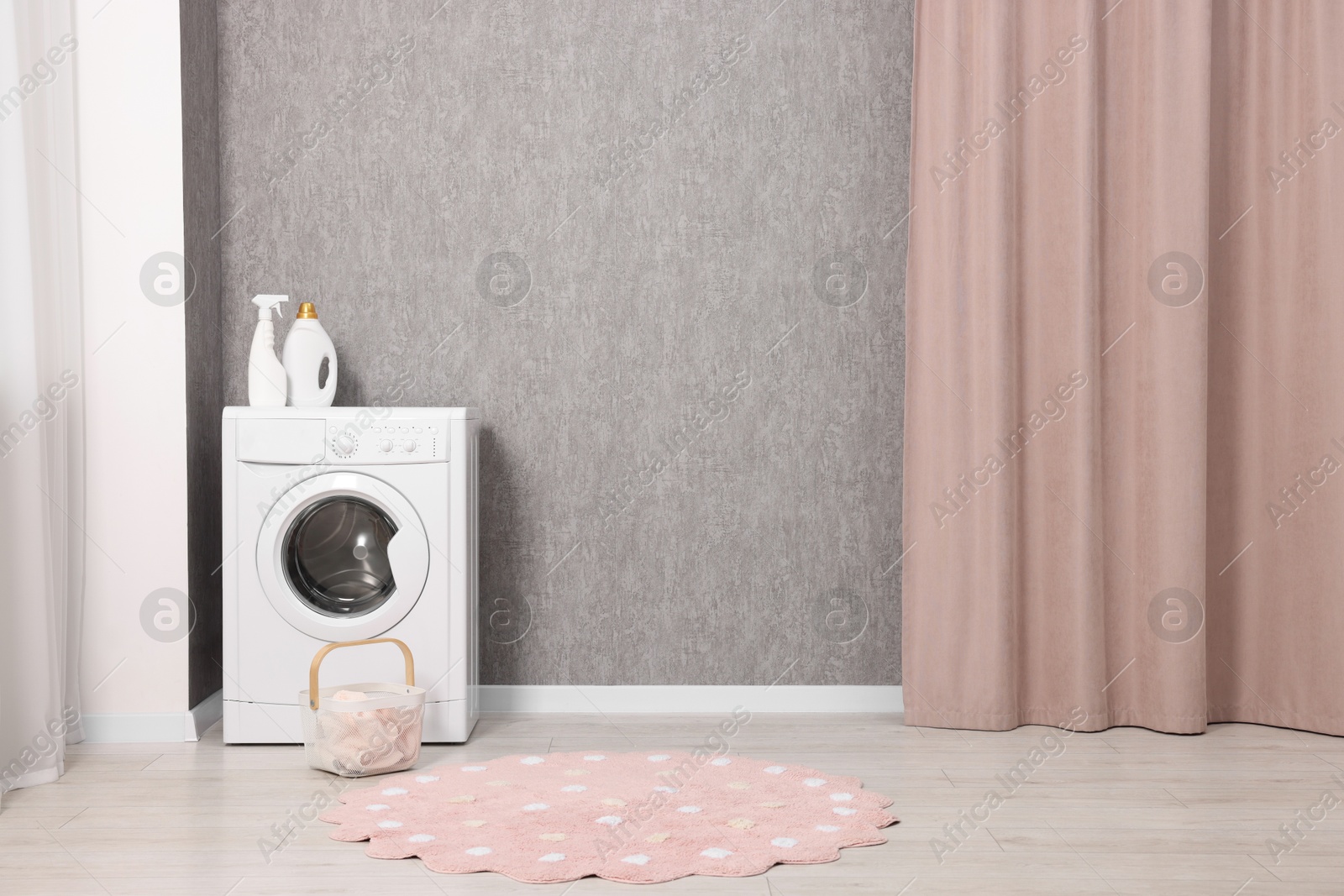 Photo of Washing machine, detergents and basket with laundry near grey wall indoors