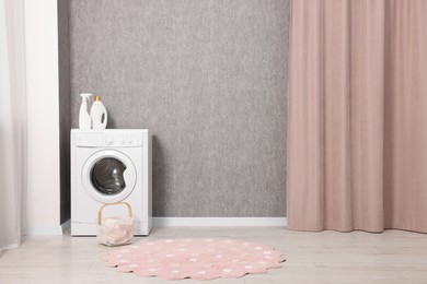 Washing machine, detergents and basket with laundry near grey wall indoors