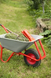 Photo of Wheelbarrow with mown grass, rubber boots and pitchfork outdoors