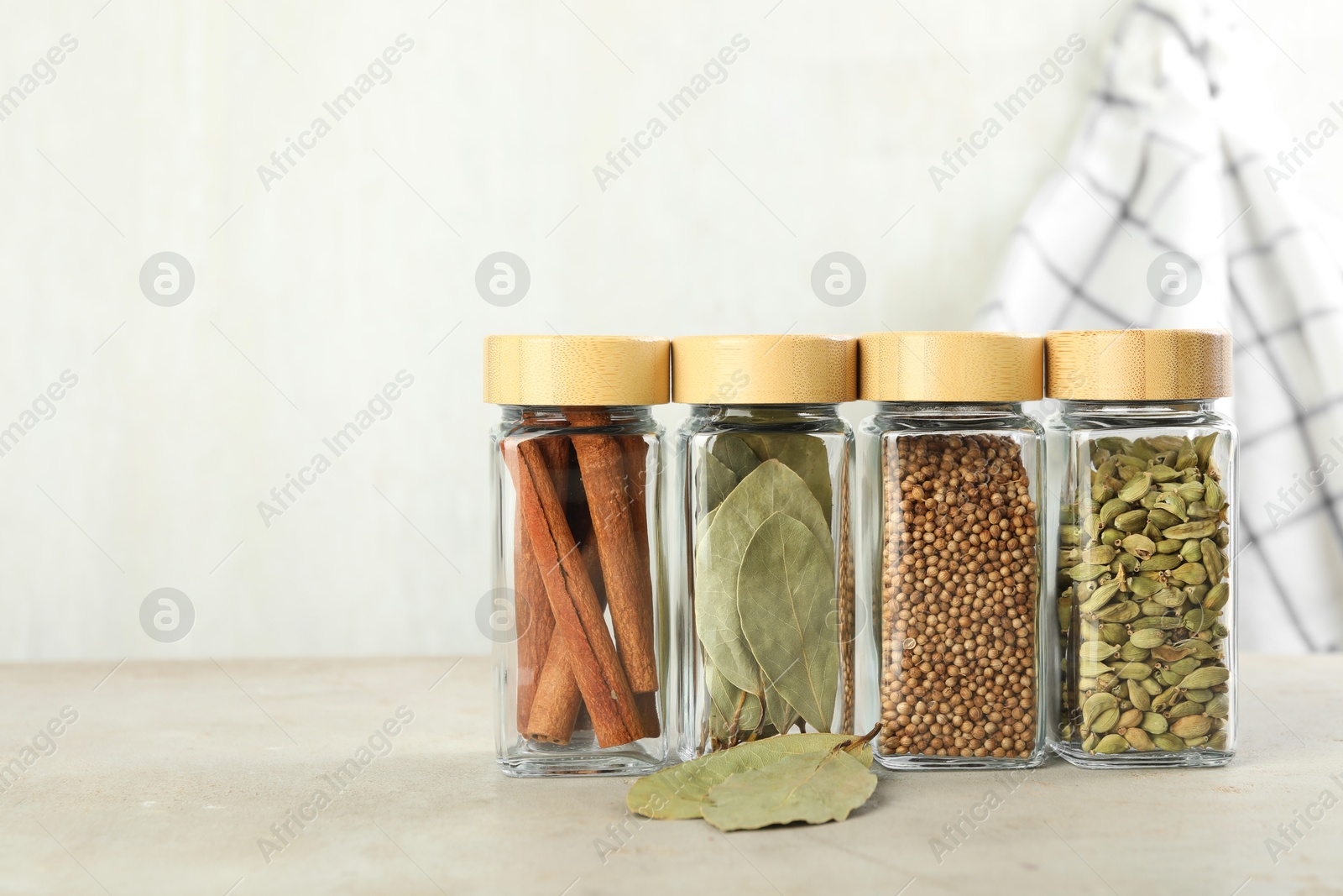 Photo of Different spices in glass jars on light textured table. Space for text