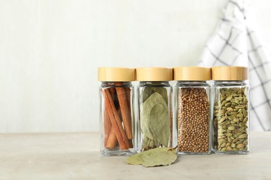 Different spices in glass jars on light textured table. Space for text