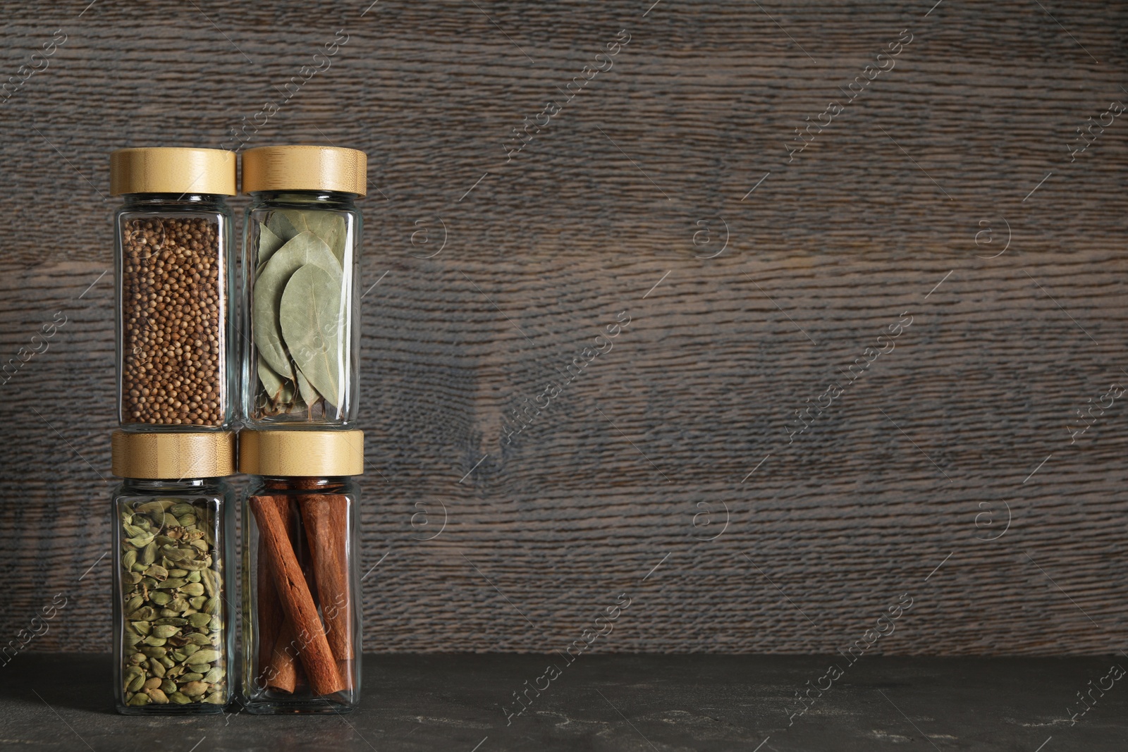 Photo of Different spices in glass jars on dark textured table. Space for text