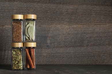 Photo of Different spices in glass jars on dark textured table. Space for text