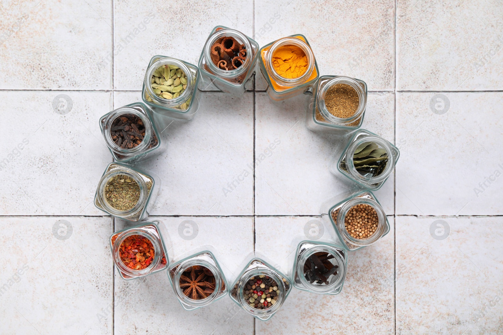 Photo of Different spices in glass jars on light tiled table, top view. Space for text