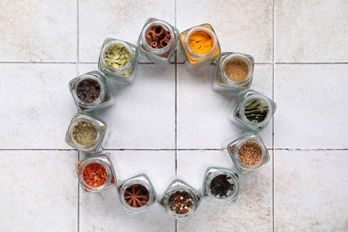 Different spices in glass jars on light tiled table, top view. Space for text