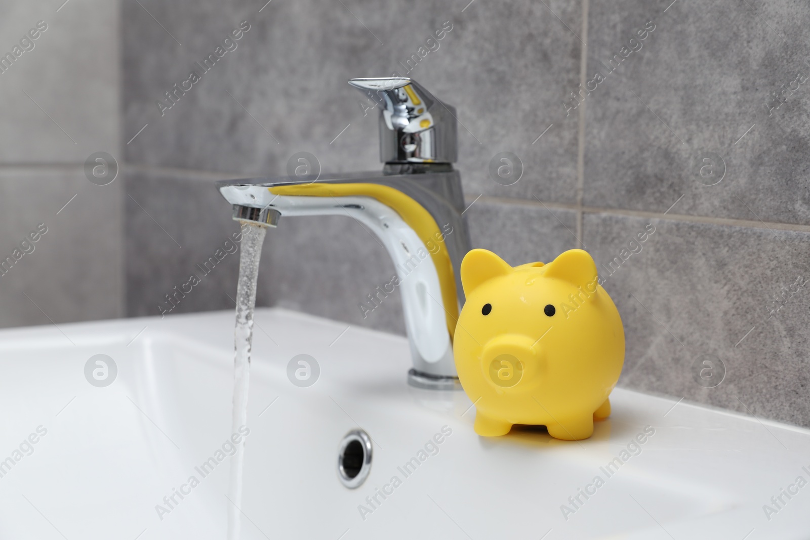 Water saving concept. Piggy bank and stream of water flowing from tap in bathroom Photo of Water saving concept. Piggy bank and stream of water flowing from tap in bathroom