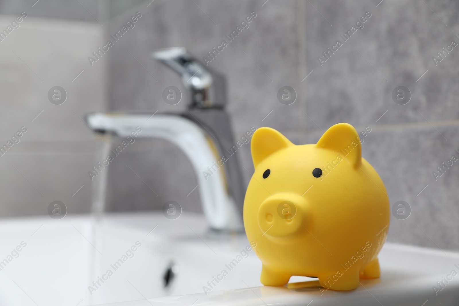 Photo of Water saving concept. Piggy bank and stream of water flowing from tap in bathroom