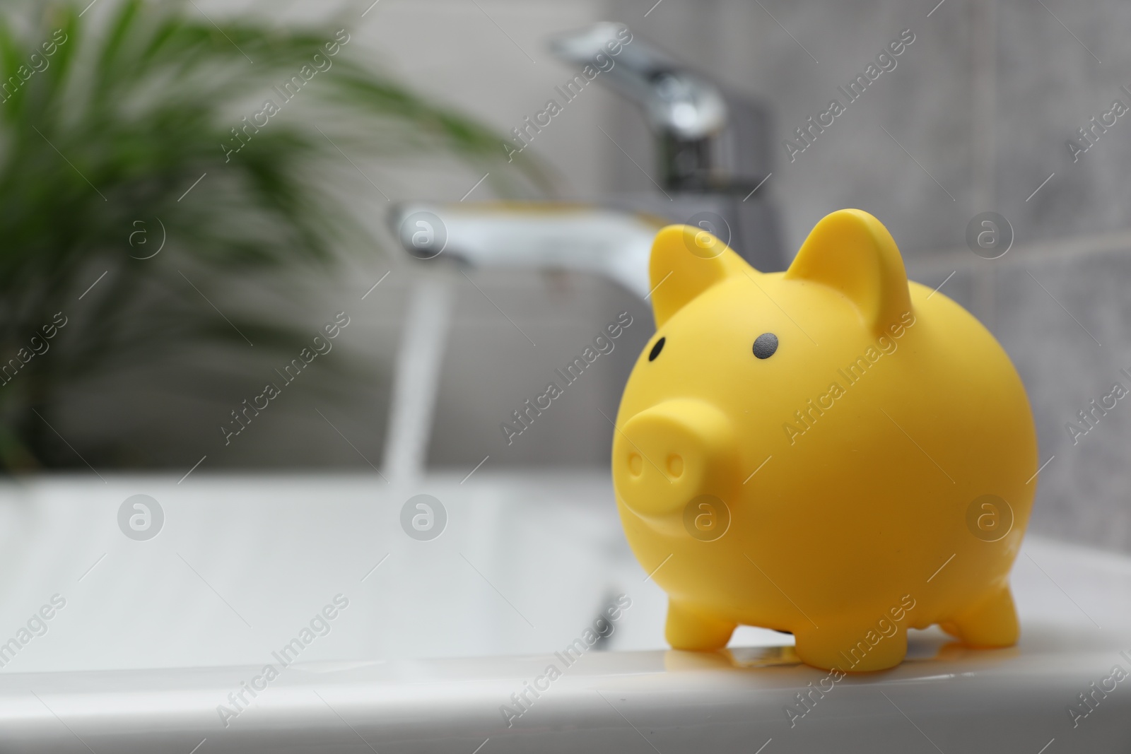Water saving concept. Piggy bank and stream of water flowing from tap in bathroom Photo of Water saving concept. Piggy bank and stream of water flowing from tap in bathroom
