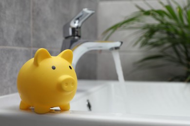 Water saving concept. Piggy bank and stream of water flowing from tap in bathroom