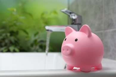 Water saving concept. Piggy bank and stream of water flowing from tap in bathroom