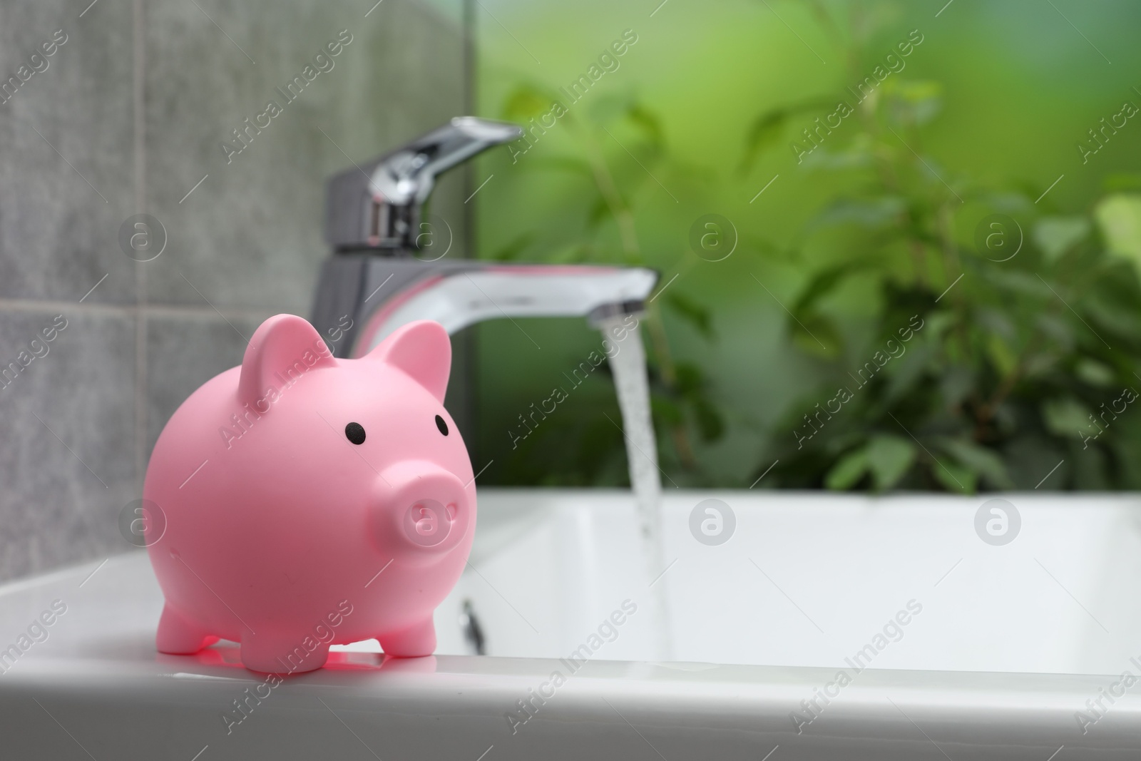 Photo of Water saving concept. Piggy bank and stream of water flowing from tap in bathroom