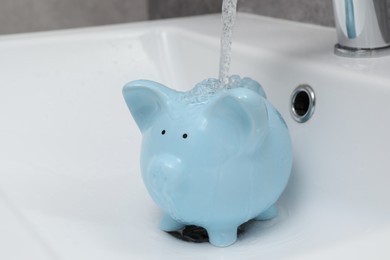 Photo of Water saving concept. Stream of water flowing from tap into piggy bank in bathroom