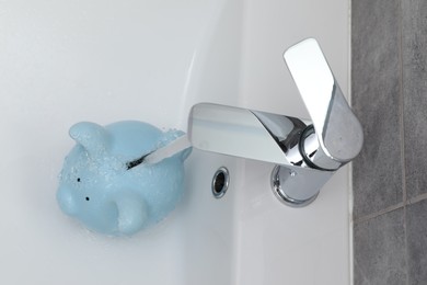 Photo of Water saving concept. Stream of water flowing from tap into piggy bank in bathroom, above view