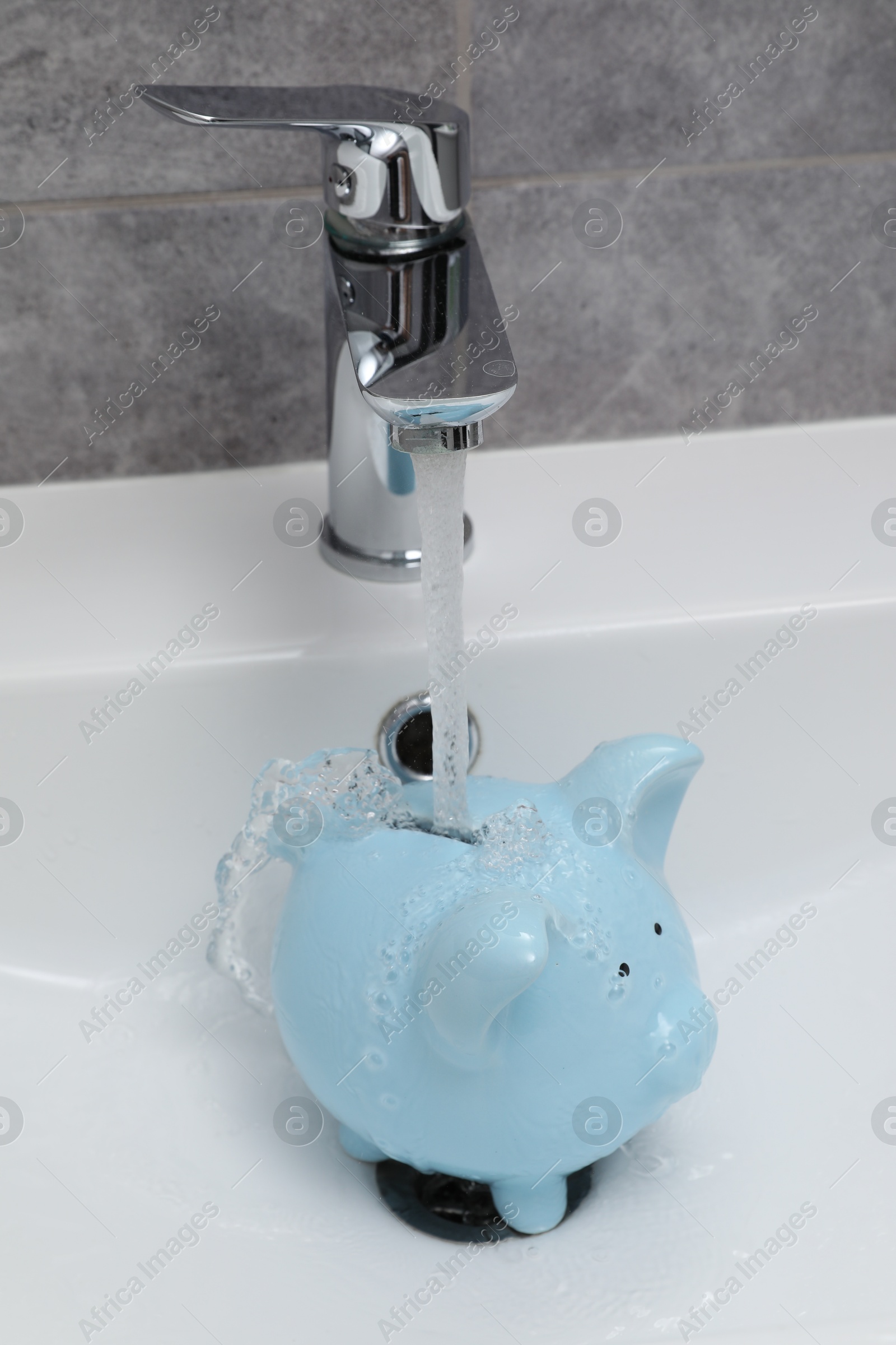 Water saving concept. Stream of water flowing from tap into piggy bank in bathroom Photo of Water saving concept. Stream of water flowing from tap into piggy bank in bathroom