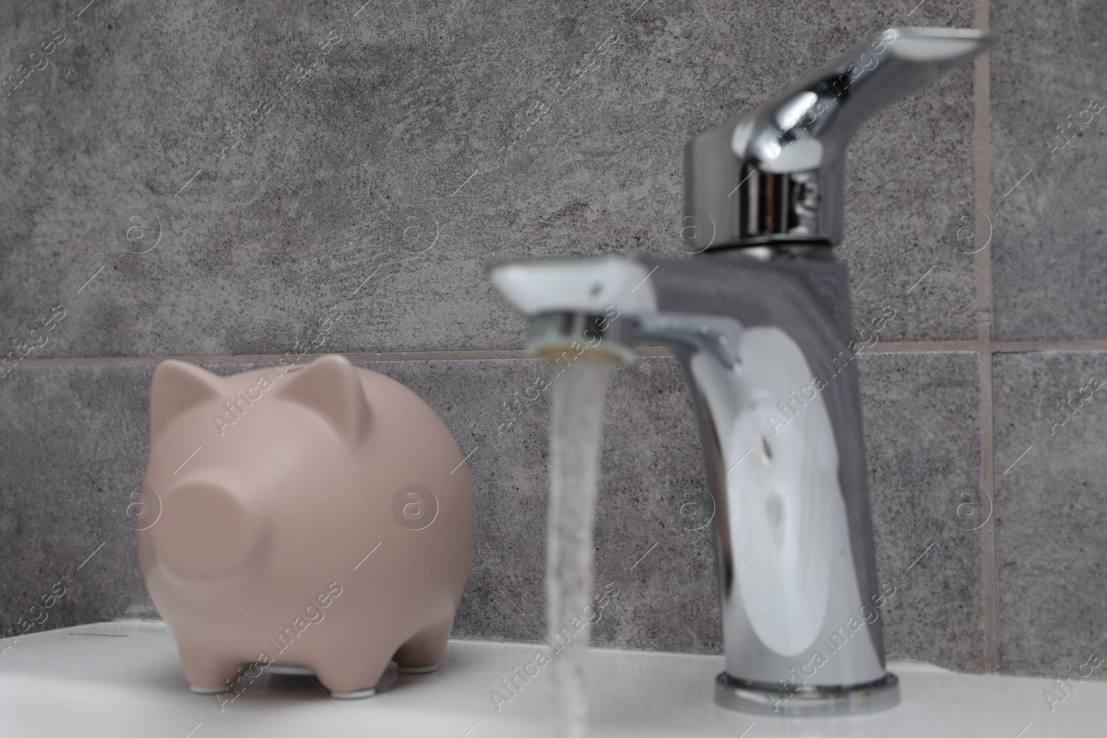 Photo of Water saving concept. Piggy bank and stream of water flowing from tap in bathroom