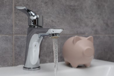 Water saving concept. Piggy bank and stream of water flowing from tap in bathroom, selective focus