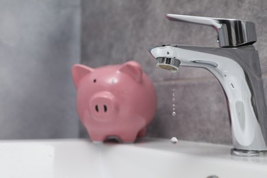 Photo of Water saving concept. Piggy bank and water drops flowing from tap in bathroom, selective focus