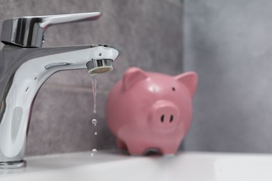 Photo of Water saving concept. Piggy bank and water drops flowing from tap in bathroom, selective focus