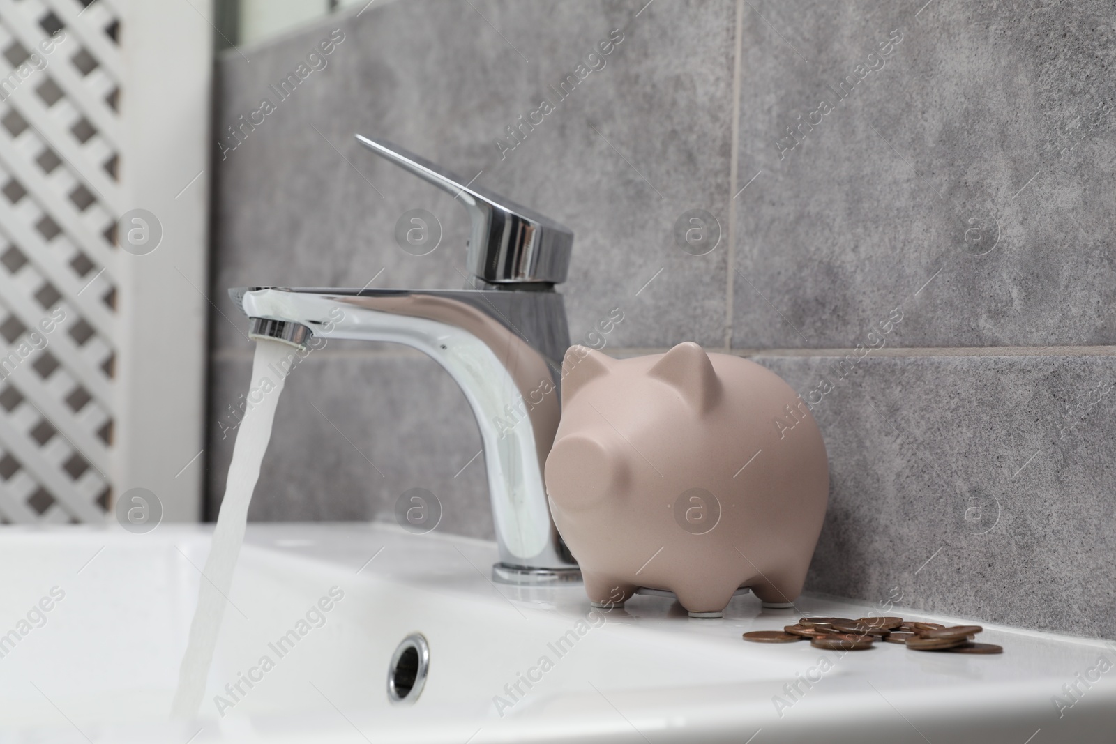 Water saving concept. Piggy bank, stream of water flowing from tap and coins in bathroom Photo of Water saving concept. Piggy bank, stream of water flowing from tap and coins in bathroom