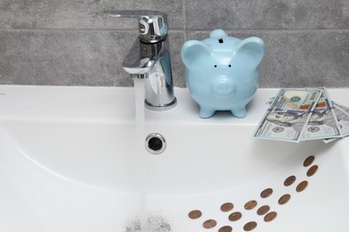 Photo of Water saving concept. Piggy bank, stream of water flowing from tap and money in bathroom