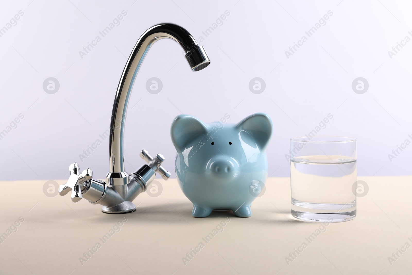 Photo of Water saving concept. Piggy bank, tap and glass of drink on pale yellow table against white background