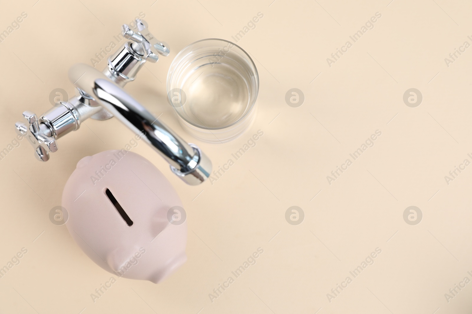 Photo of Water saving concept. Piggy bank, tap and glass of drink on pale yellow background, flat lay. Space for text