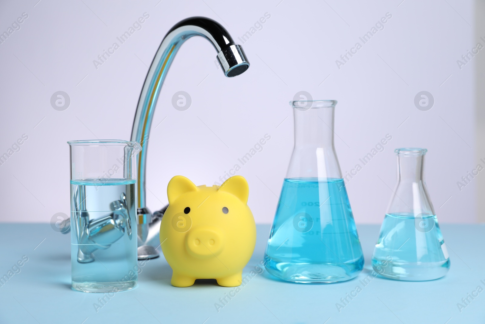 Water saving concept. Piggy bank, tap and glassware with liquid on light blue table against white background Photo of Water saving concept. Piggy bank, tap and glassware with liquid on light blue table against white background