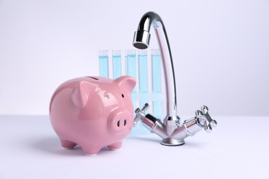 Photo of Water saving concept. Piggy bank, tap and test tubes with liquid on white background