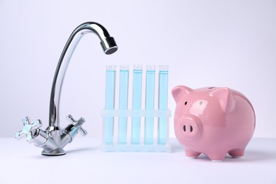 Photo of Water saving concept. Piggy bank, tap and test tubes with liquid on white background