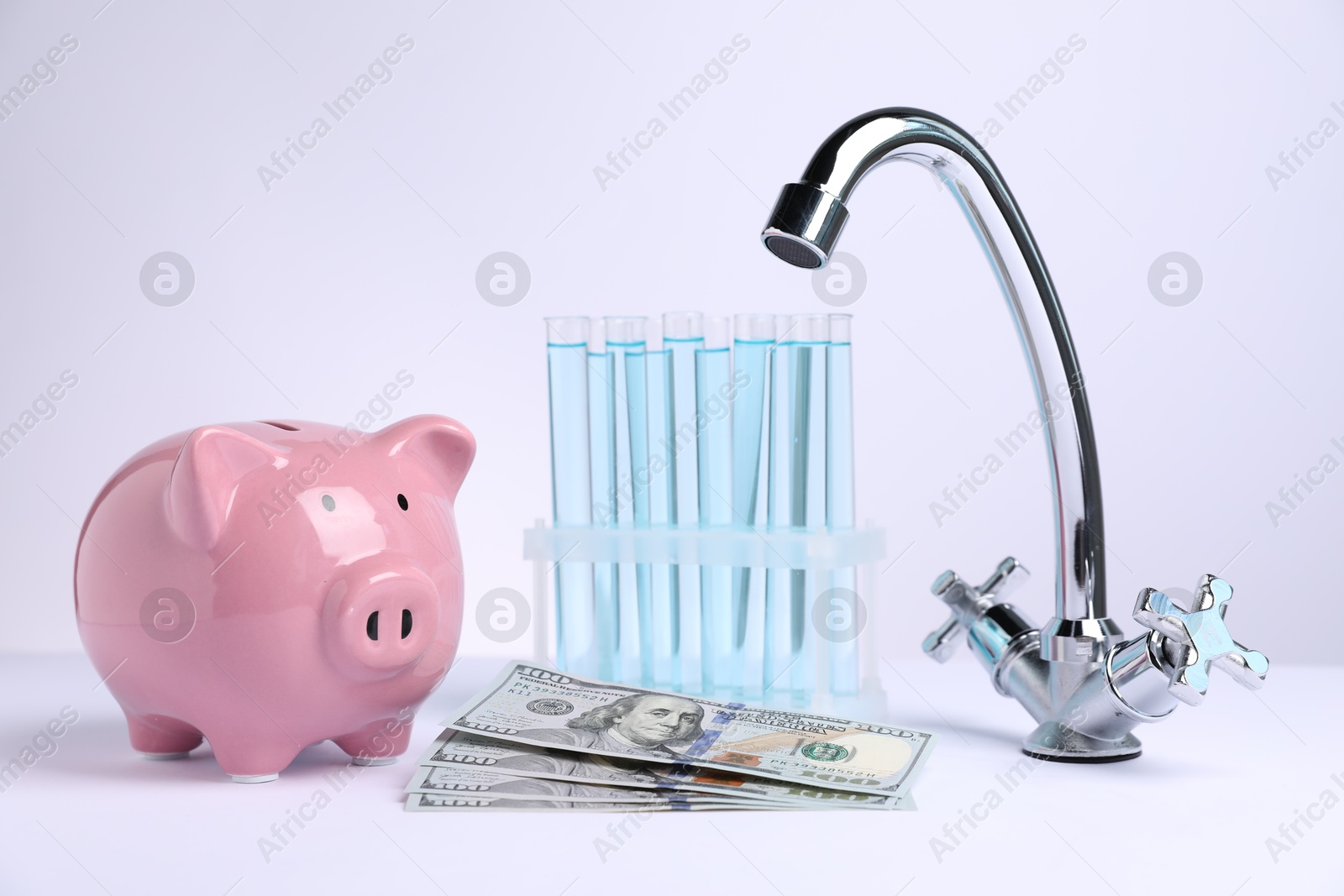 Photo of Water saving concept. Piggy bank, tap, test tubes with liquid and dollar banknotes on white background