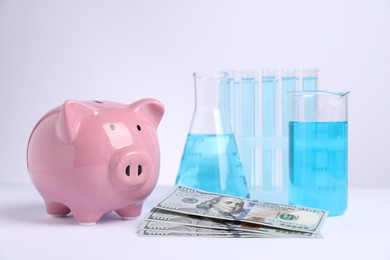 Photo of Water saving concept. Piggy bank, glassware with liquid and dollar banknotes on white background