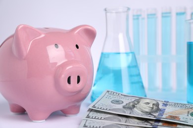 Photo of Water saving concept. Piggy bank, glassware with liquid and dollar banknotes on white background, closeup