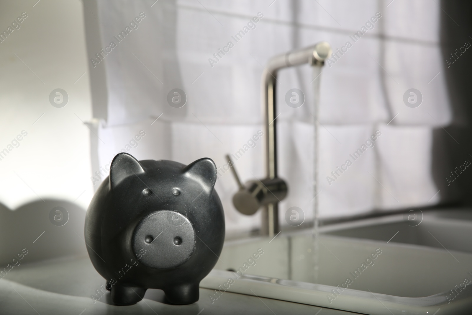 Water saving concept. Piggy bank and stream of water flowing from tap in kitchen Photo of Water saving concept. Piggy bank and stream of water flowing from tap in kitchen