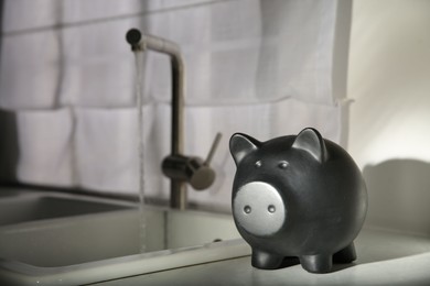 Photo of Water saving concept. Piggy bank and stream of water flowing from tap in kitchen