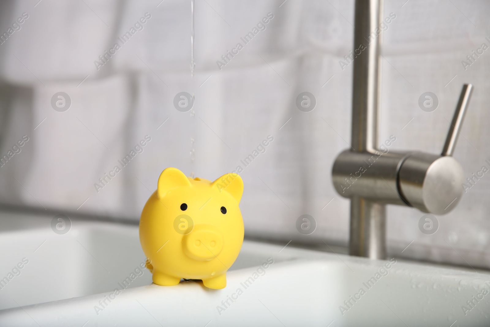 Water saving concept. Stream of water flowing from tap into piggy bank in kitchen Photo of Water saving concept. Stream of water flowing from tap into piggy bank in kitchen